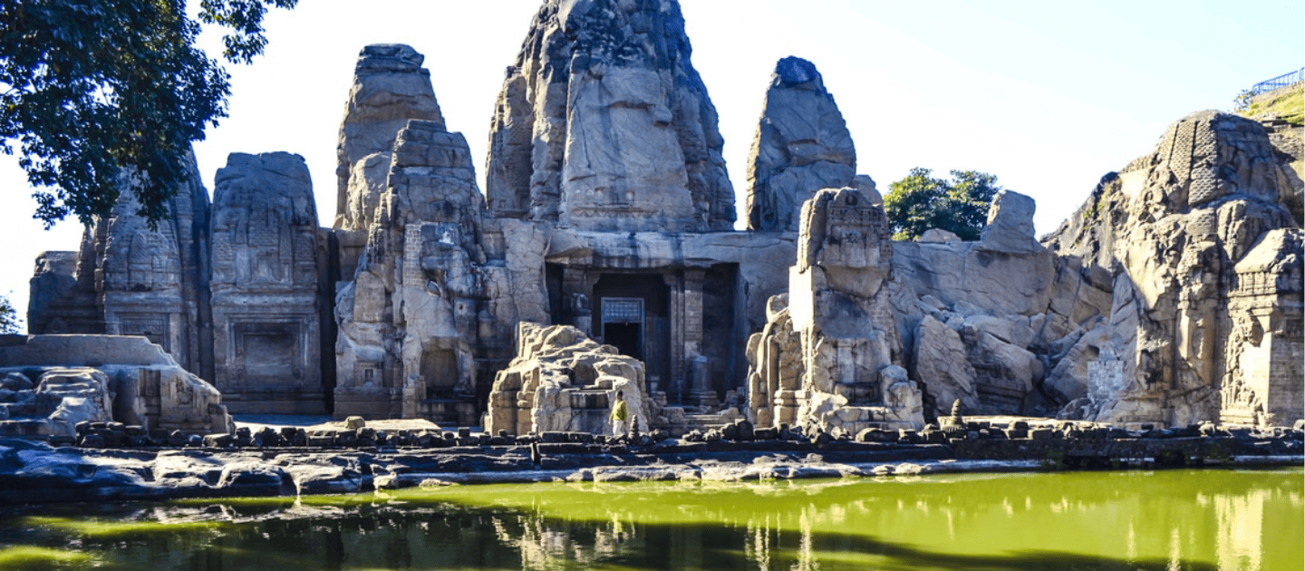 Scenic view of the 8th-century Masrur Rock Cut Temples in Kangra, Himachal Pradesh, featuring ancient monolithic rock-cut architecture and a sacred pond in the foreground