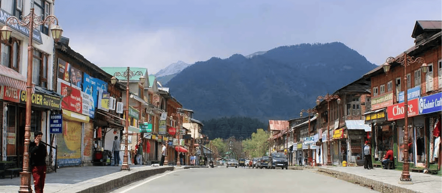 View of the main market street in Pahalgam lined with local handicraft shops, hotels, and scenic mountains in the background