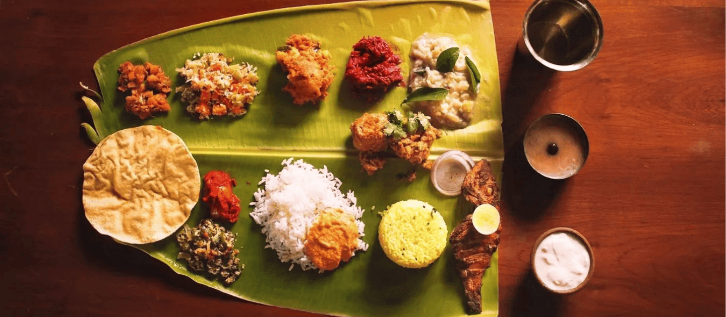 Traditional South Indian feast served on a banana leaf, featuring white and yellow rice, vegetable stir-fries, spicy chutneys, fish fry, and lentil curry, representing authentic Thanjavur cuisine