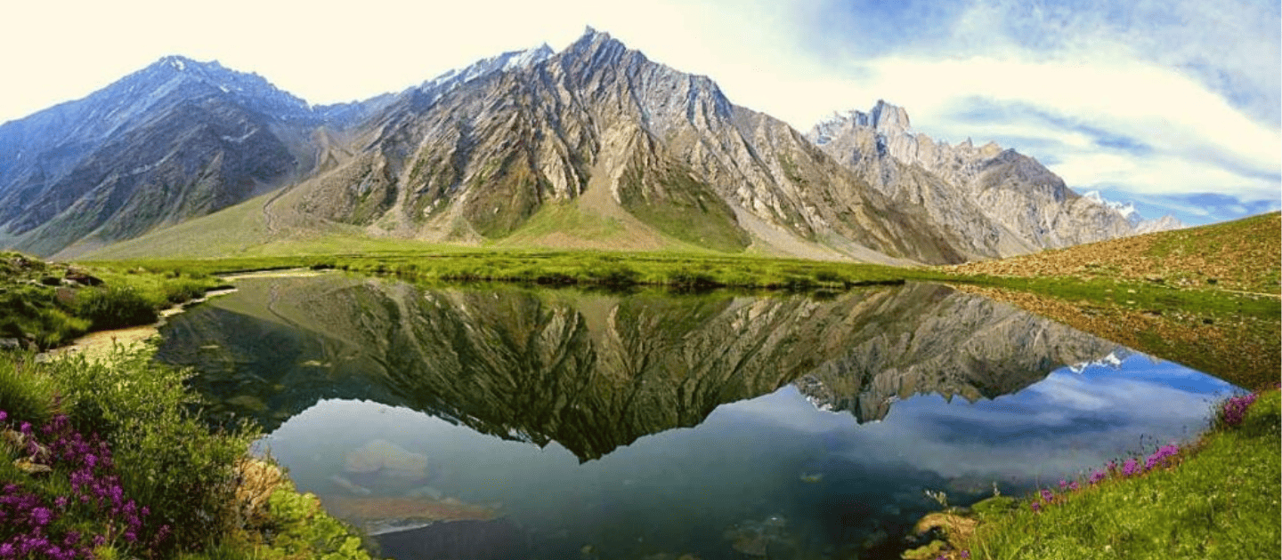 A beginner solo traveler's view of a pristine mountain lake with a perfect reflection of jagged peaks and green meadows.
