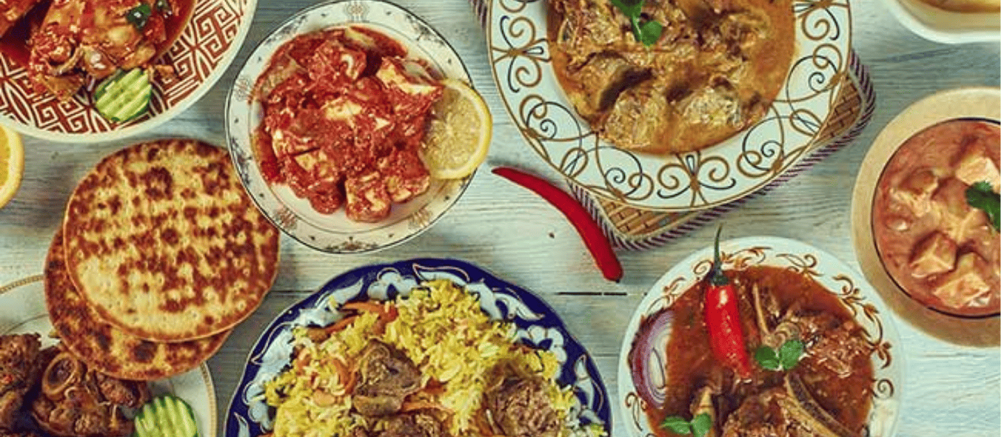 Top view of a traditional Kashmiri Wazwan feast featuring aromatic dishes like Rogan Josh, saffron rice, paneer, and fresh flatbreads served in ornate bowls