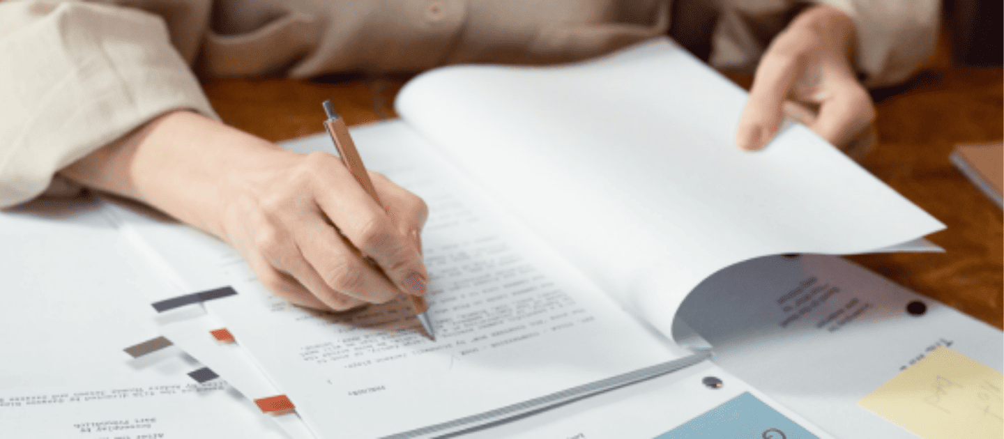 Close-up of a travel planner writing on a document, symbolizing the detailed customization of a trip itinerary, reviewing a travel contract, or finalizing a booking checklist