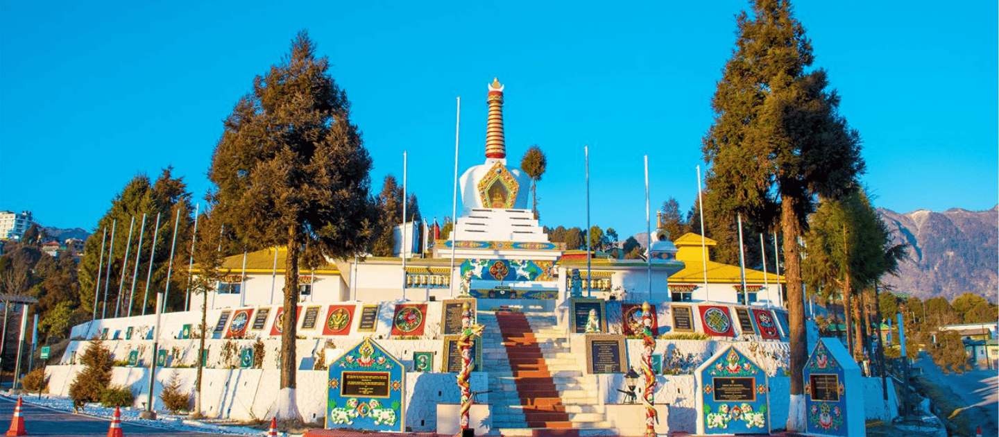 Scenic view of the Tawang War Memorial stupa surrounded by tall pine trees and mountains under a clear blue sky